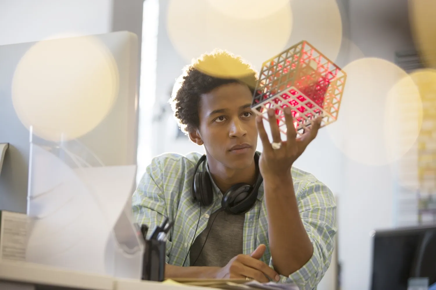 A young man in deep thought. He is looking at a cube that he is holding in his hand.