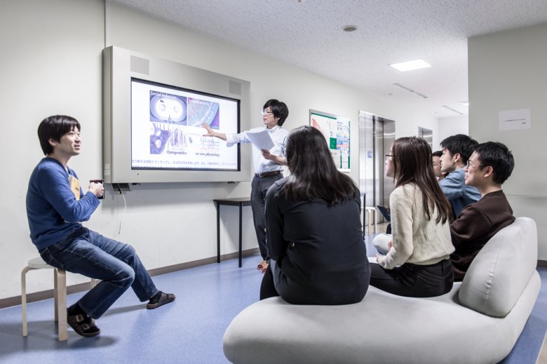 People sitting in front of a screen on the wall, talking.