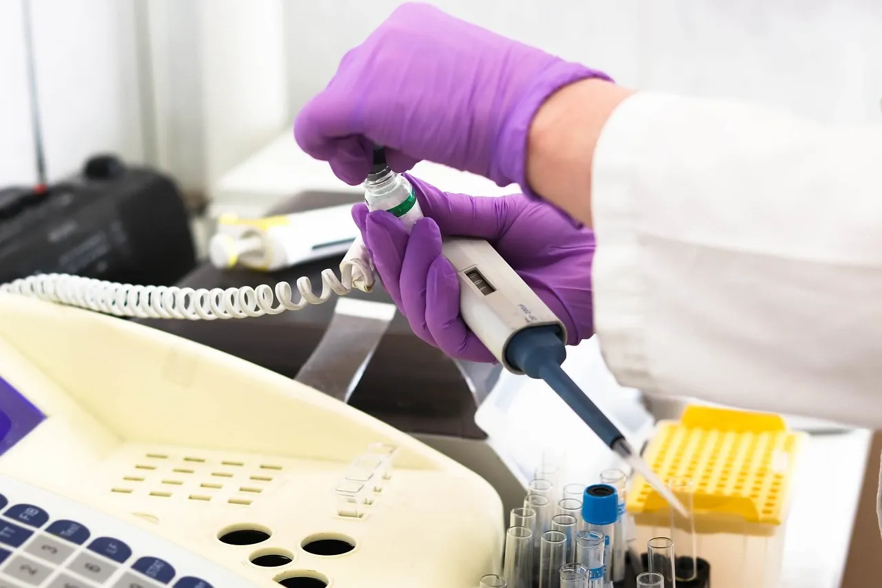 gloved hands in a lab holding a small glass vial