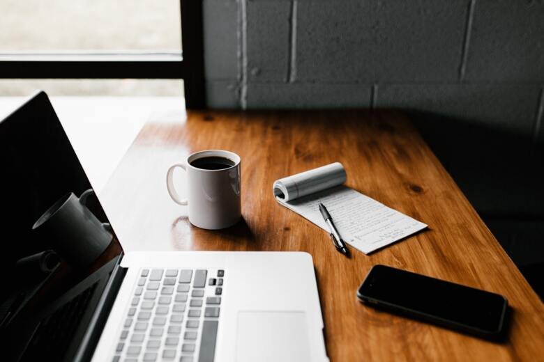 MacBook, coffee cup, note and smartphone on a desk.