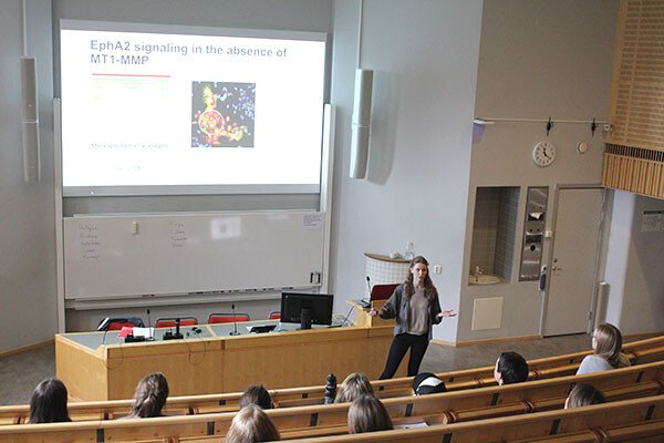 View over a lecture hall, teacher is presenting on the screen while students are sitting in their chairs listening