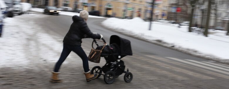 Person med barnvagn går över en vintrig innerstadsgata.