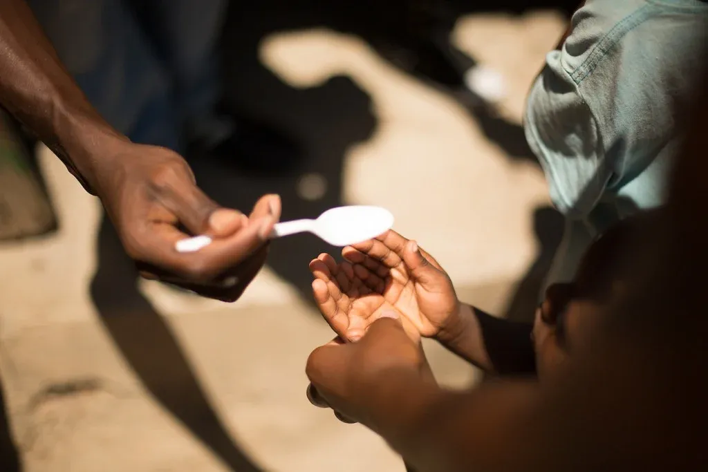 One hand holding a white spoon over two hand together.