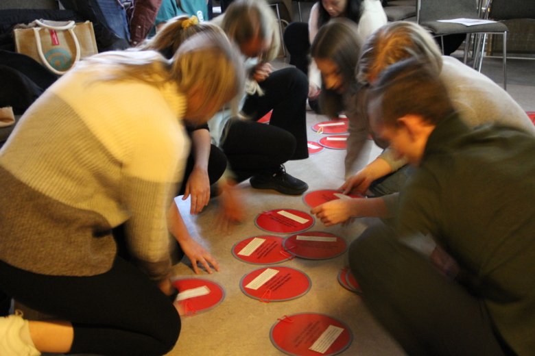 personer på huk på golvet sorterar röd platta cirklar som symboliserar patienter