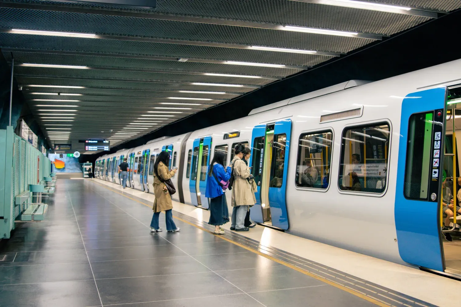 Commuters wait at a Stockholm metro station platform with a train ready for boarding.
