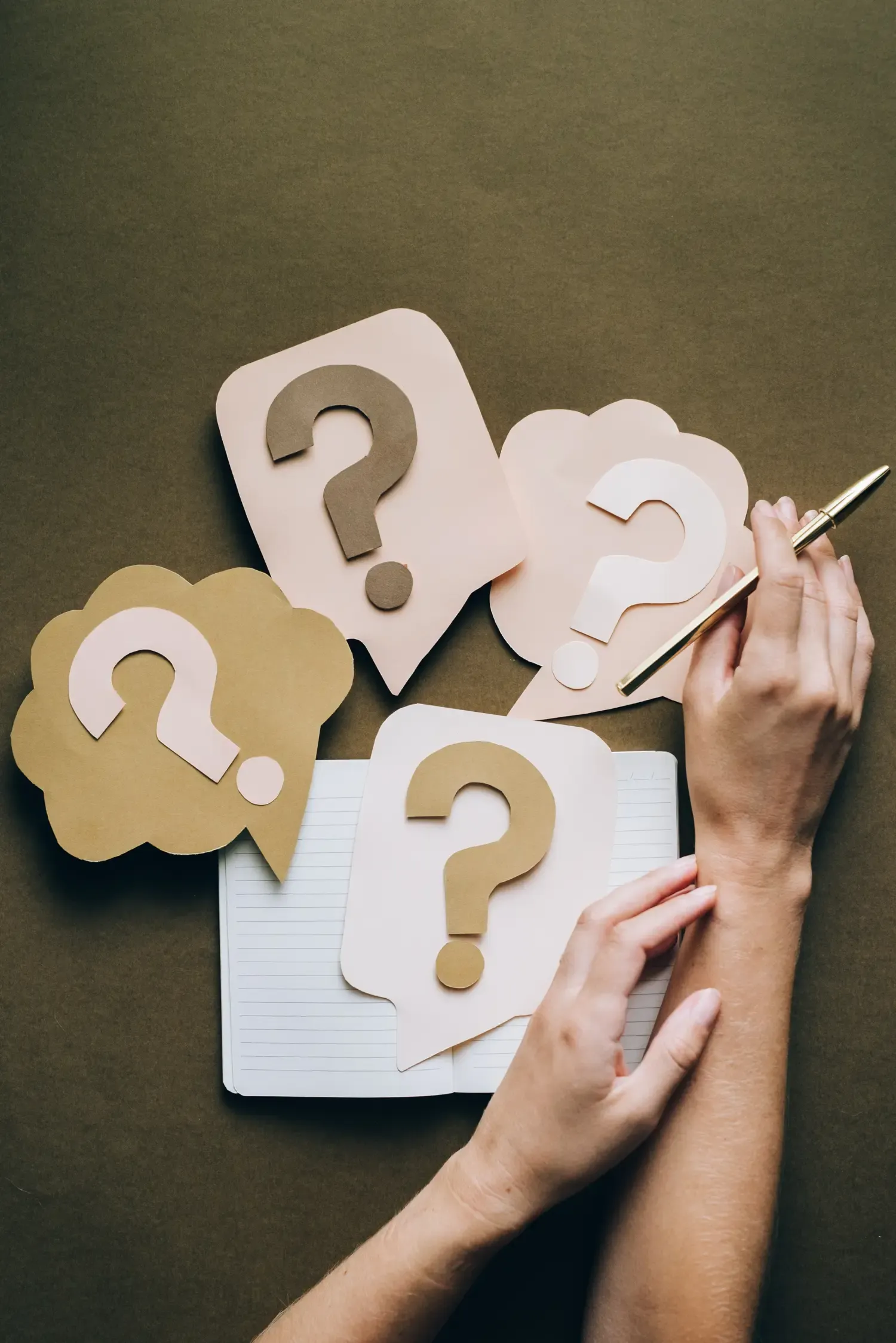 An image of a notepad and a person holding a pen, along with several question marks.
