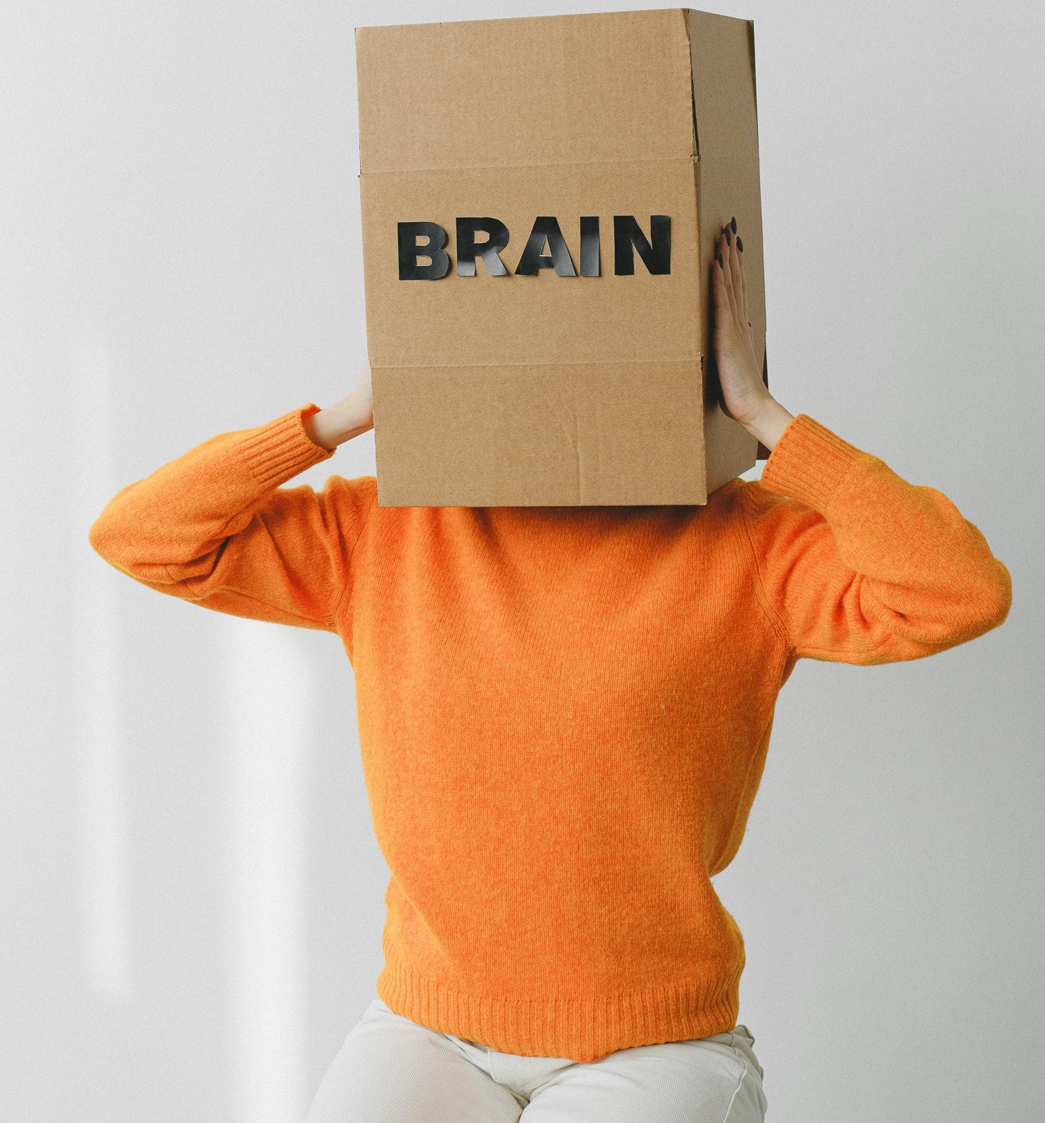 Person wearing an orange sweater with a cardboard box over their head, with the word “BRAIN” written on the front.