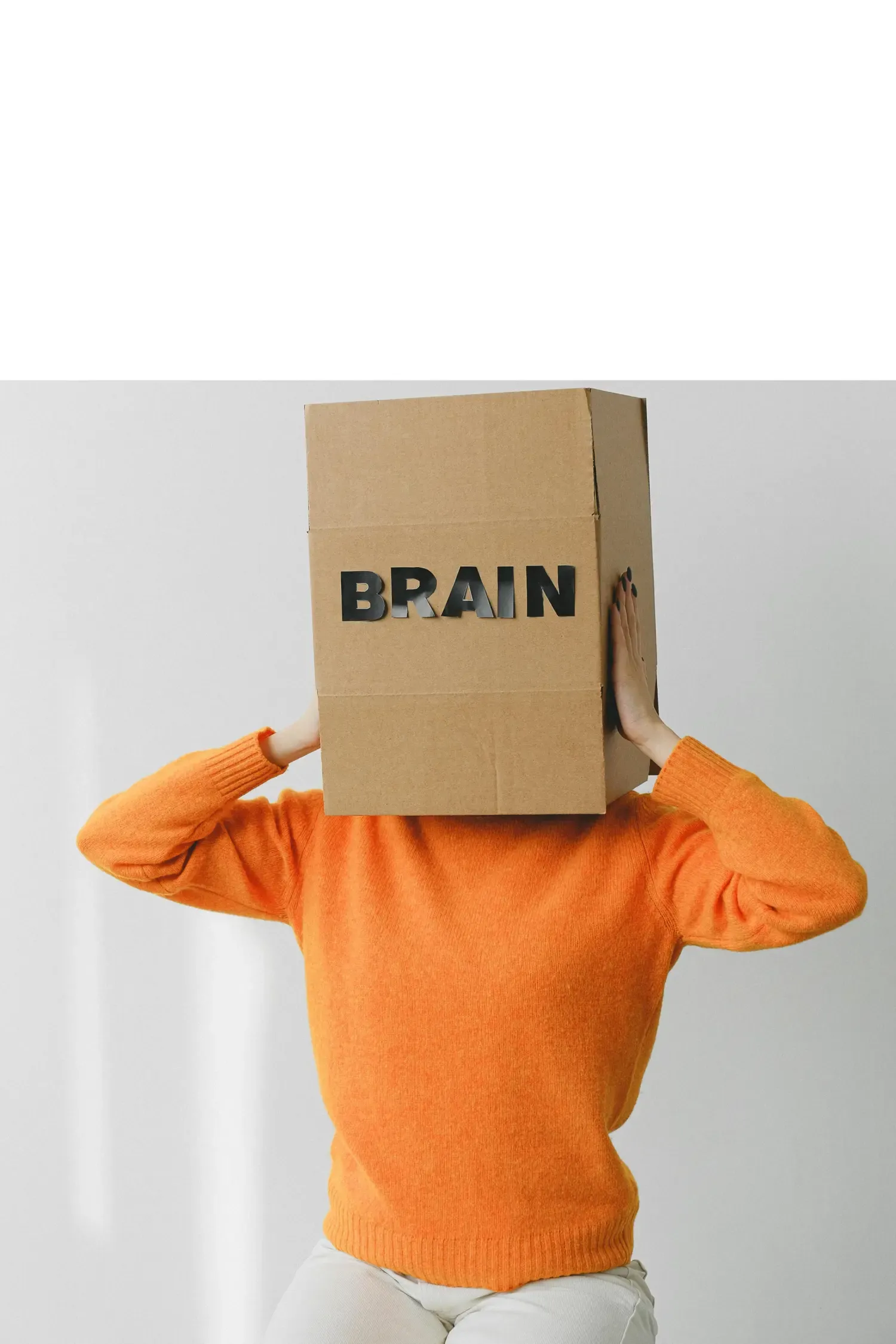 Person i orange tröja med en kartong över huvudet, där ordet “BRAIN” står skrivet på framsidan.