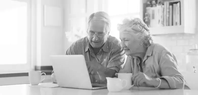 Äldre par som sitter vid ett bord och tittar på en bärbar dator.