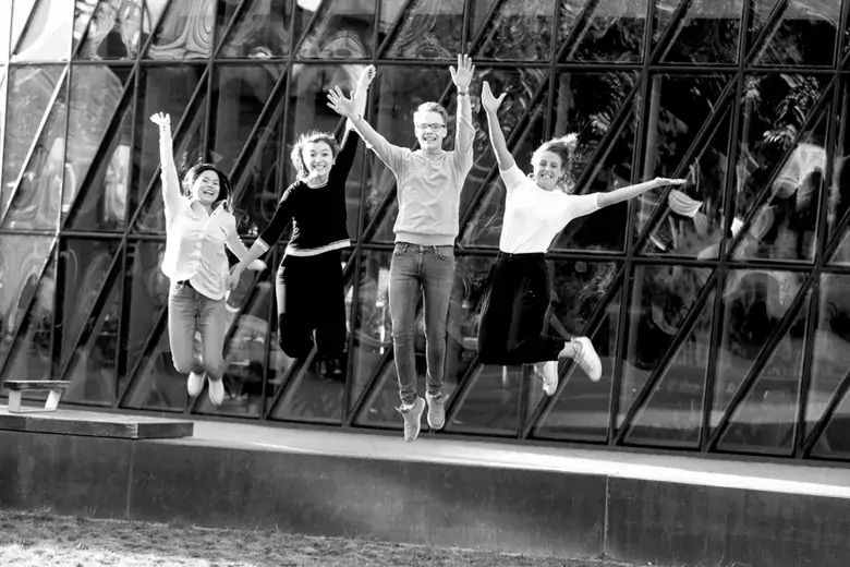 four students jumping in the air by the main entrance of Aula Medica, Solna