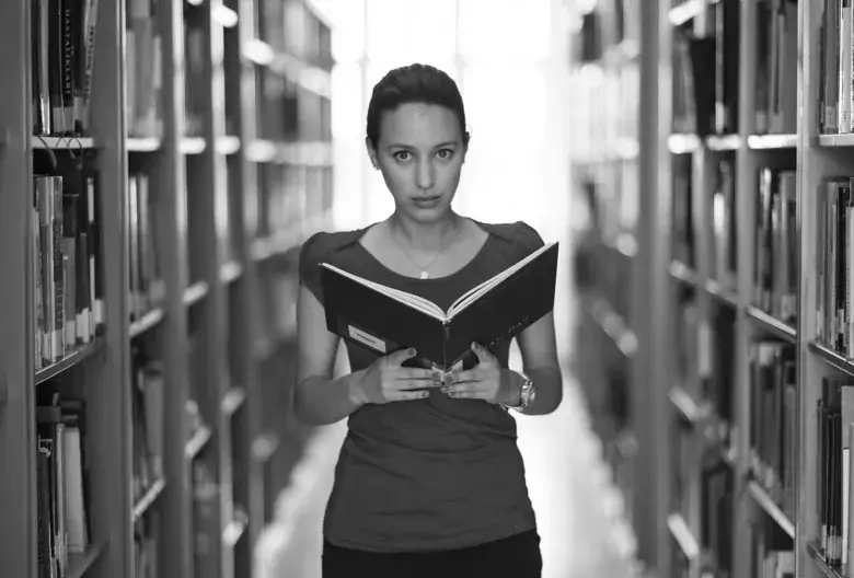 Kvinna läser bok i bibliotek.