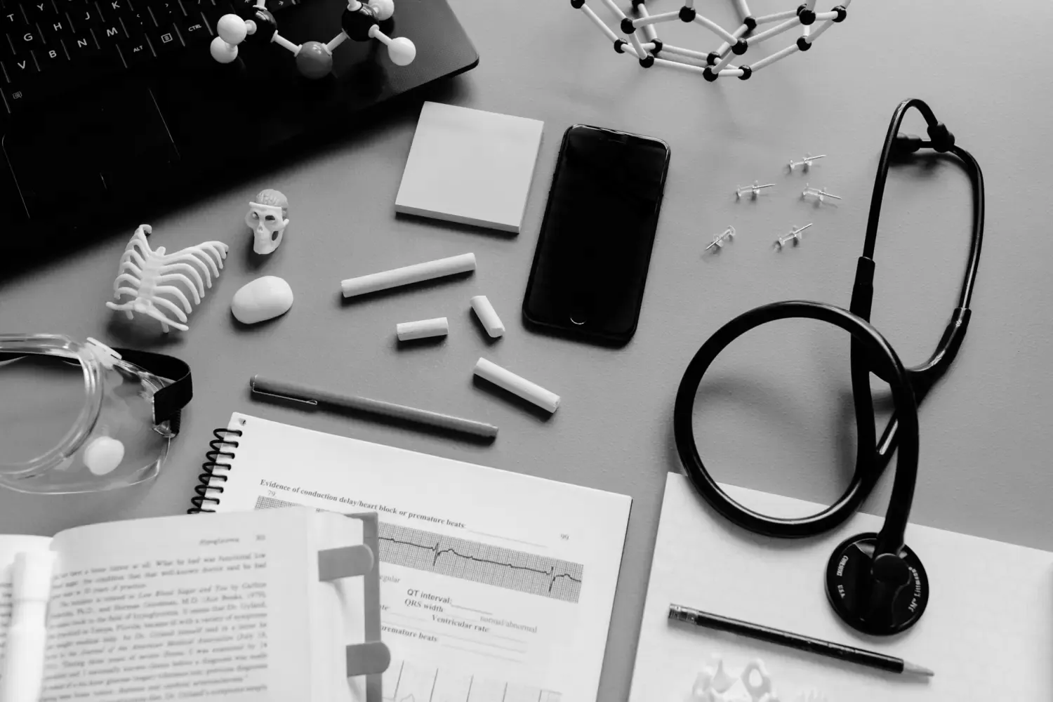 a desk filled with paper, tacs, a phone, laptop, stetoskope and more