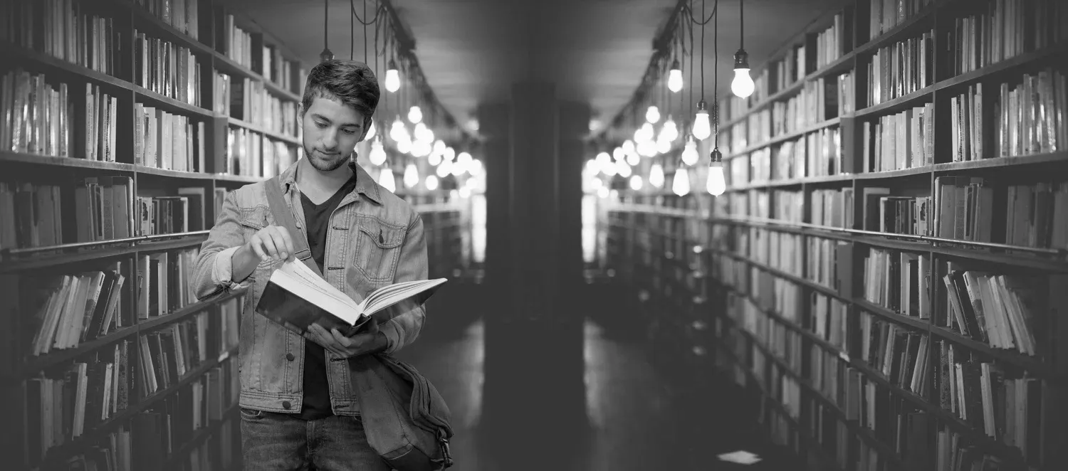 Student läser bok i bibliotek.