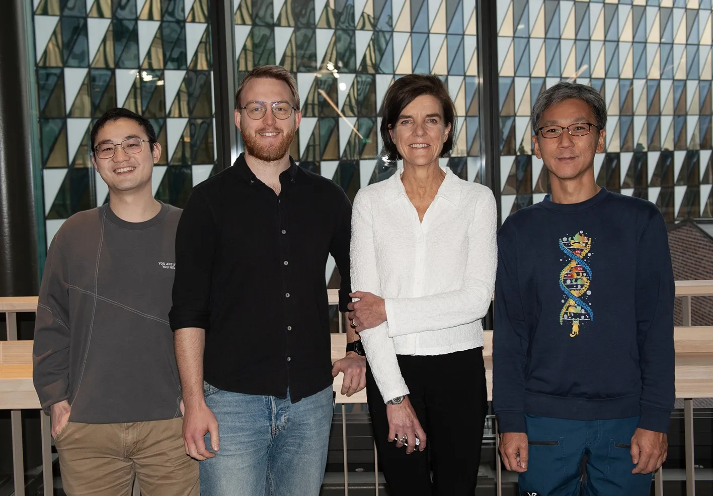 Four people on a row smiling, aula medica in the background.