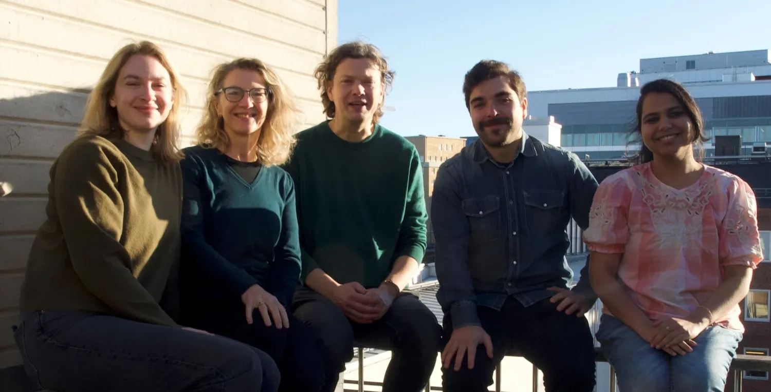 Five people are sitting on a balcony. In the background, you can catch a glimpse of the New Karolinska Hospital in Solna
