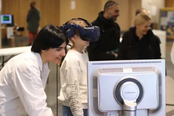 Esra Öncel stands next to a young visitor who is wearing VR-glasses and testing her balance in various challenges.