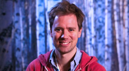 Portrait of Eric Thelin against blue backdrop in a red hoodie.