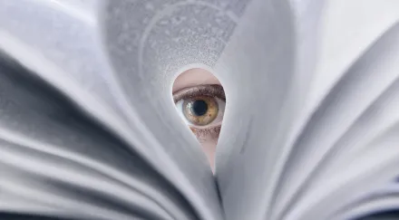 An eye looking through a folded book page.