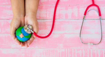 Symbolic illustration: hands holding a globe, which is being examined with a stethoscope.