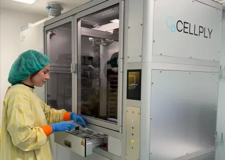 A researcher in a yellow coat stands next to a laboratory machine.