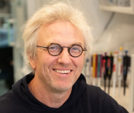 A portrait of a smiling man. He is wearing glasses and a black sweatshirt.