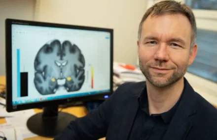 Andreas Olsson in fron av creen with an image of a brain.