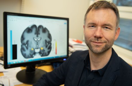 Andreas Olsson in fron av creen with an image of a brain.