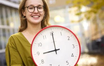 Researcher Theresa Lemke holding a clock displaying 9 am.