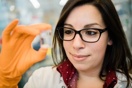 Scientist wearing rubber gloves, holding up a small glass container.