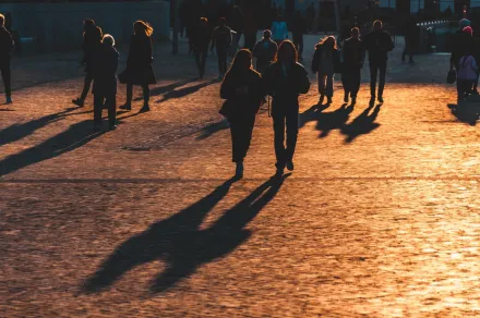 En mångfaldig grupp silhuetter vandrar på solbelysta kullerstenar och kastar långa skuggor under den gyllene timmen.