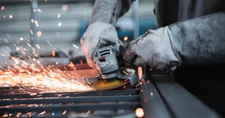 Hands in work gloves holding a grinder that sprays sparks.