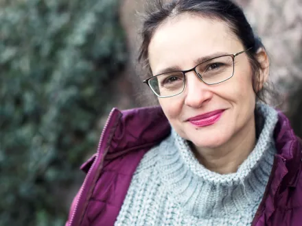 Porträtt av Nicoleta Eserblom, lutad mot en stenvägg. Foto: Rebecka Uhlin.