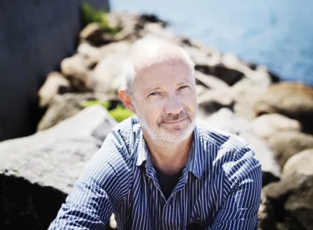 porträttbild av Fredrik Tjulander sittandes på klippor vid havet, vid en pir.