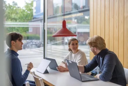 Tre studenter som sitter och pratar och studerar tillsammans på campus