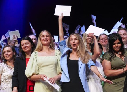 Studenter på Erling Persson-scenen ler, firar och viftar med sina kuvert.