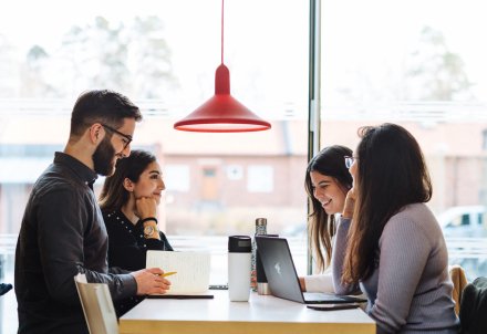 Four students sitting around a table and talking. || Four students with their laptops studying. || students studying || Students in group work