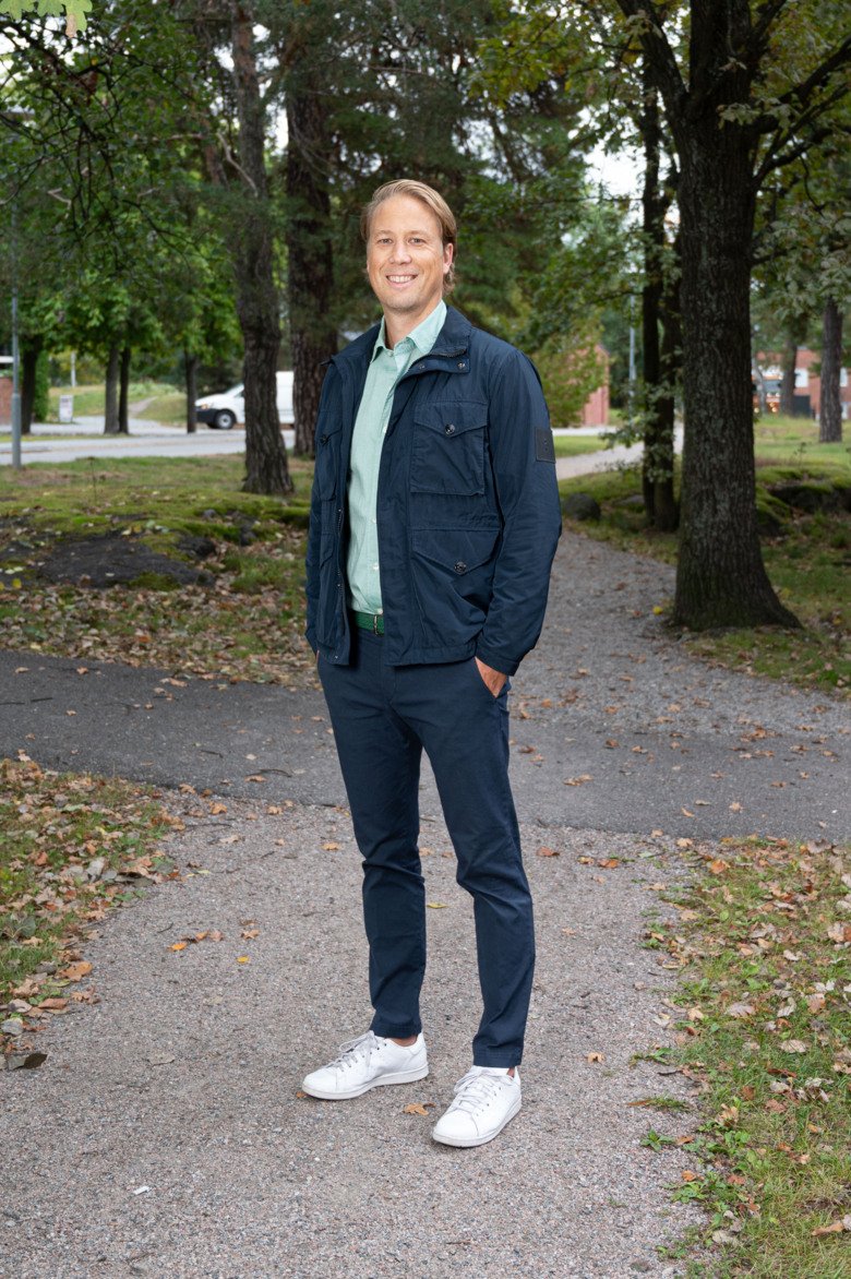 Porträtt av Eric Westman, han ler och står på en gångväg i en park.